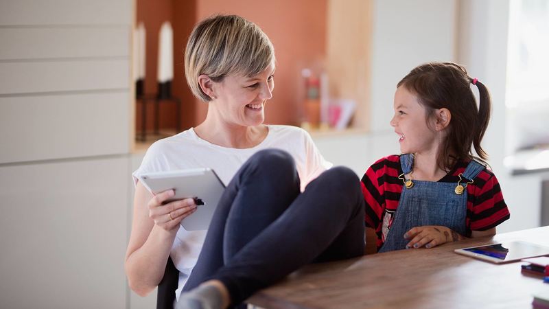 Mor og datter smiler til hverander, mens mor holder en tablet.