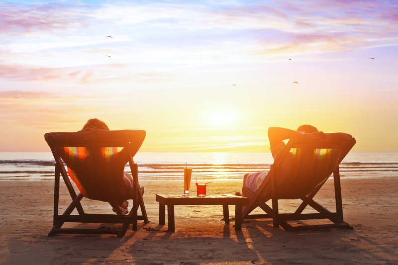 To personer i fluktstoler på en strand skimtes mot en solnedgang